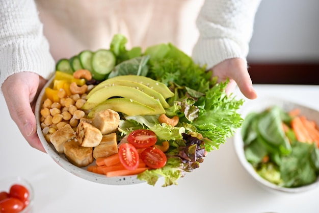 A female holding a plate of Buddha bowl or plant based salad vegetables mixed closeup image