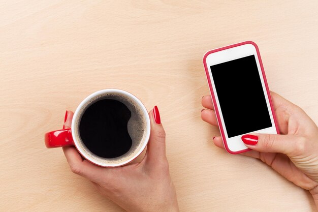 Female holding smartphone and coffee cup top view with copy space