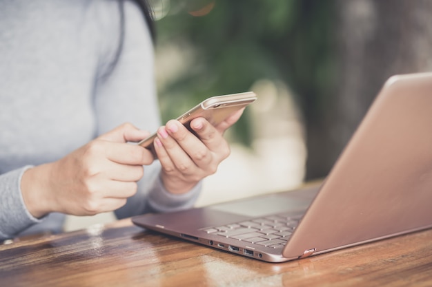 Female holding smartphone getting message with confirmation making transaction on laptop computer