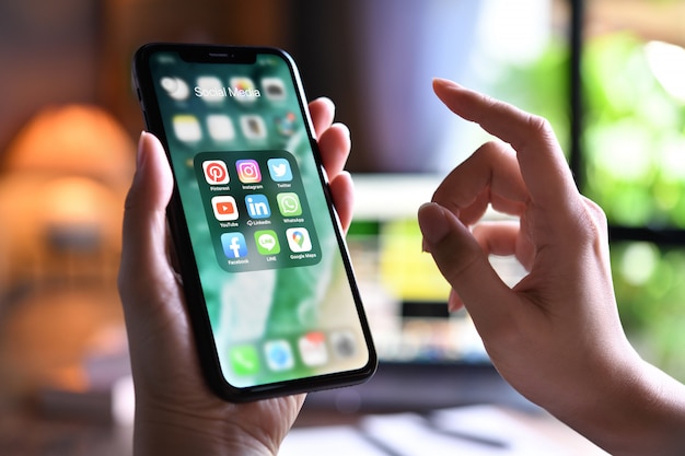 Photo female holding a smartphone with icons of social media on the screen at home