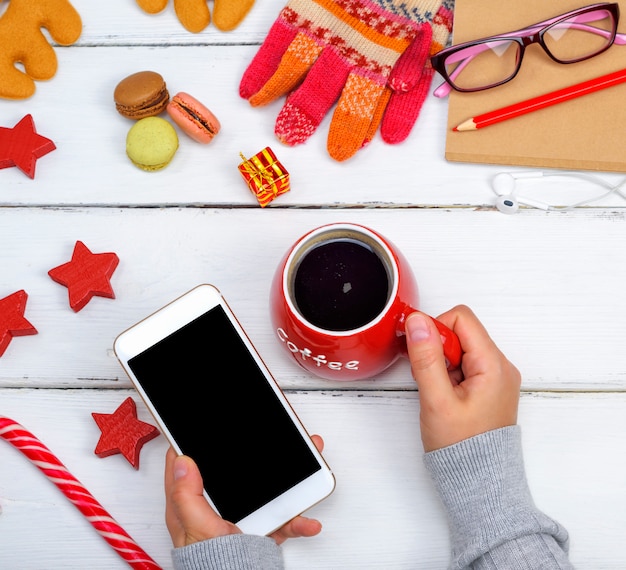 A female holds a phone with a black blank screen, and in the other hand a red cup of coffee 