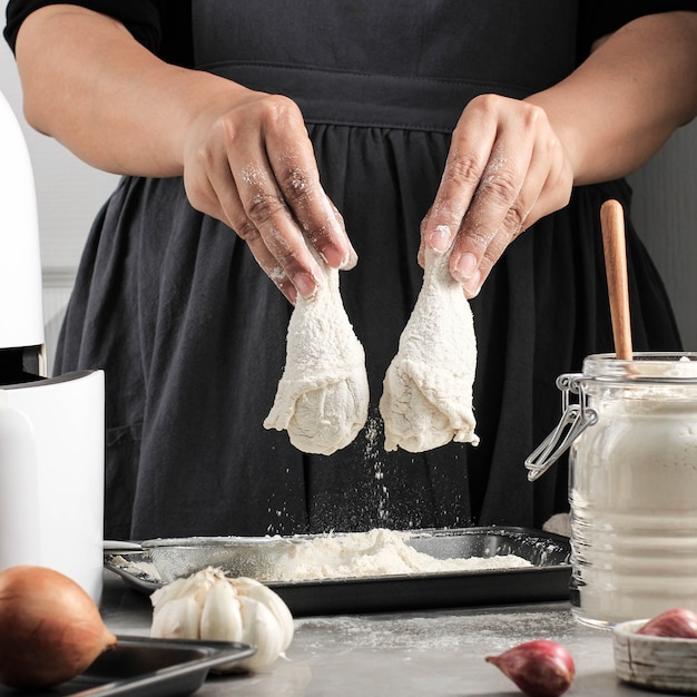 Cuoco domestico femminile che prepara pollo fritto croccante fatto in casa, ricoprendo le cosce di pollo con farina in cucina