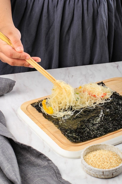 Female home maker put japcahe stir fry glass noodle on nori\
seaweed. step by step making kimmari or gimmari, korean popular\
street food snack