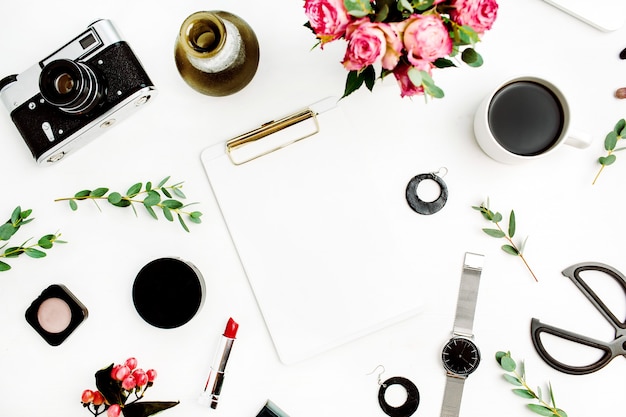 Female home office workspace with clipboard, laptop, rose flowers, eucalyptus branches, fashion accessories and cosmetics. Flat lay, top view