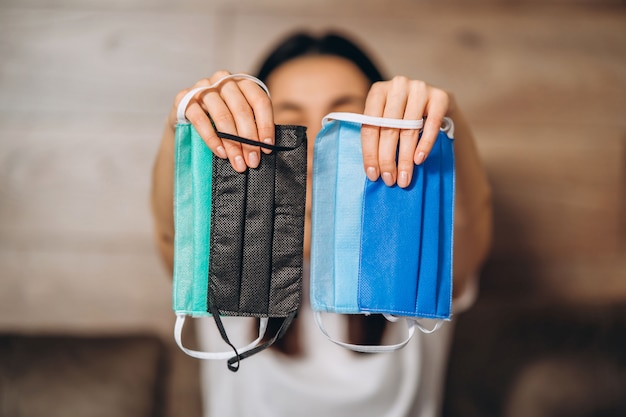 Female at home in quarantine time holding colorful protective medical masks to prevent virus disease