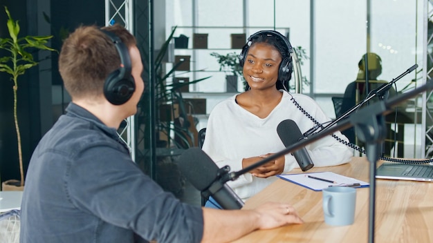 Female host talking to a guest friend on a podcast radio\
station in the studio african american and european record podcast\
and discuss social issues business radio show