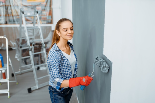 L'imbianchino femminile in guanti dipinge il muro. riparazione della casa, donna ridente che fa lavori di ristrutturazione dell'appartamento, ristrutturazione della stanza