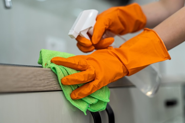 Female housekeeping hands in gloves cleaning counter top in kitchen close up cleaning concept