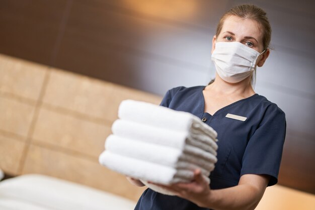 Cameriera femminile in piedi con asciugamani freschi e puliti durante la pulizia della camera d'albergo. concetto di servizio alberghiero. copia spazio