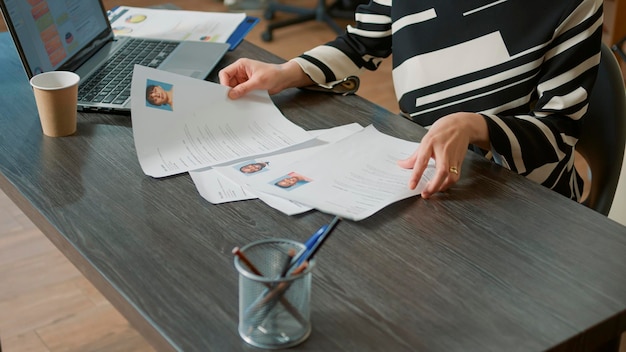 Female HR employee looking at cv resume to hire candidates, analyzing information before job interview. Woman using expertise documents to make job offer and recruit applicants. Close up.