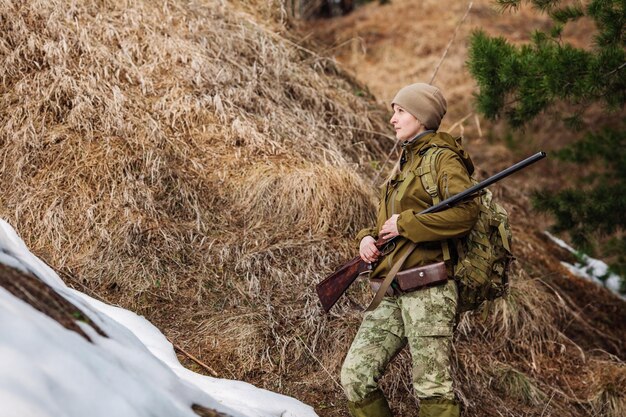 Female hunter in camouflage clothes ready to hunt holding gun and walking in forest