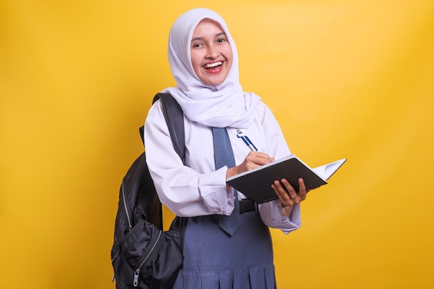 Female indonesian high school student in white and grey uniform holding book and pen