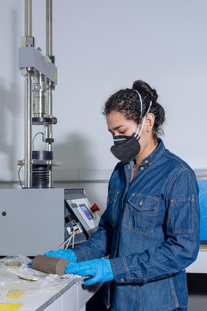 Female industrial worker with protective mask and blue latex gloves in a geological testing laboratory unpacking a clay cylinder