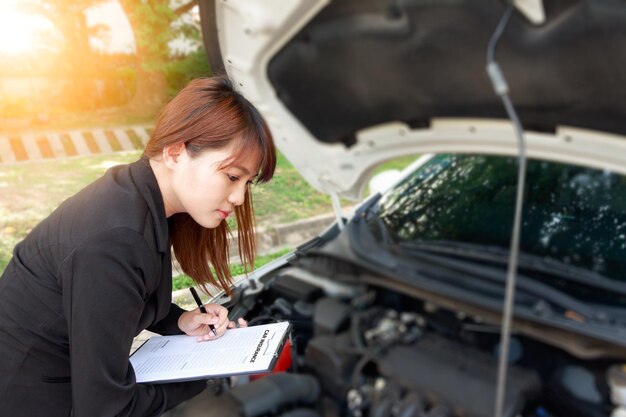 Foto agente assicurativo femminile che controlla il motore dell'auto mentre fa rapporto