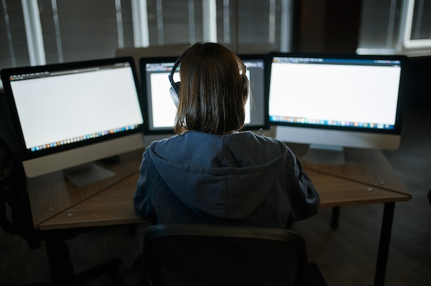 Женский интернет-хакер в наушниках работает на компьютере в темном офисе. Незаконный веб-программист на рабочем месте, преступное занятие. Взлом данных, кибербезопасность