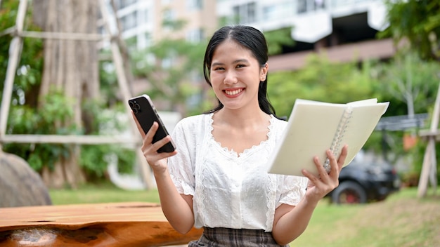 A female is holding a book and her smartphone while relaxing in an outdoor garden