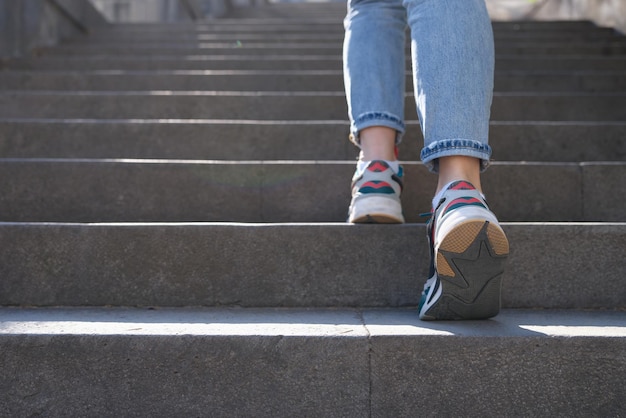 Female in jeans and sneakers going up steep stairs