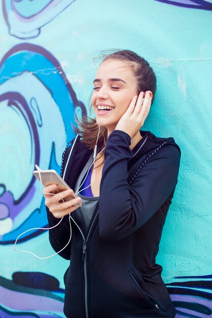 Female jogger listening music on mobile phone in front of graffiti wall