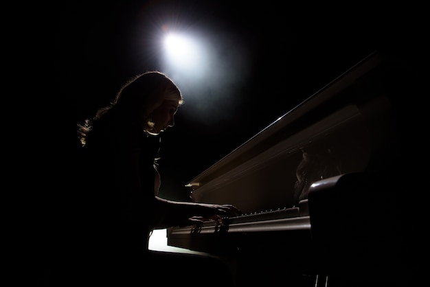 Female keyboards player on stage during concert, backlight