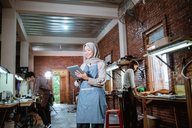 Photo female leather craftsman in veil using digital tablet in studio