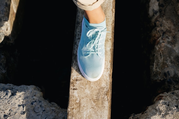 Female legs in beige pants and sneakers are on the board over the cliff