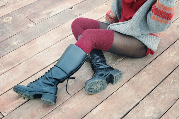 Female legs dressed in knee high boots and knitted stockings, woman sitting on a wooden planking, winter outdoor