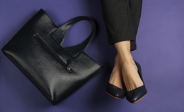female legs dressed in trousers and classic shoes with heels and bag on purple background. top view. beauty and fashion studio shot