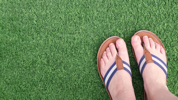 Female legs in flat leather sandals on a green artificial turf