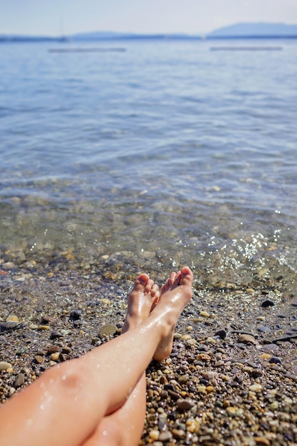 Photo female legs a girl is sunbathing on pebble beach of geneva lake summer vacations and travel