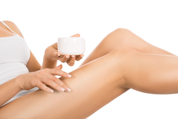 Female legs and hands with a jar of cream. Woman applying moisturizer on her perfect legs, isolated on white background.