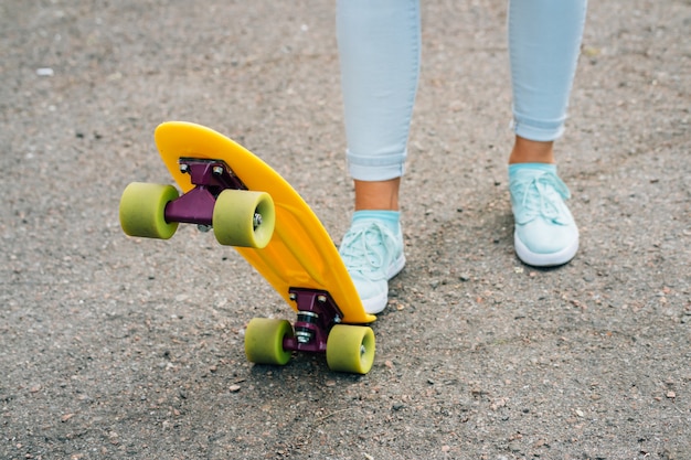 Gambe femminili in jeans e scarpe da ginnastica in piedi vicino a brillante giallo skateboard