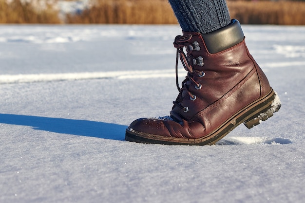 革の茶色の防水ブーツの女性の足は、新雪を踏む。カジュアルファッション、流行の靴。