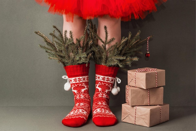 Gambe femminili in calze di lana rosse con ornamenti, rami di abete e regali di natale su sfondo verde. buon natale o capodanno, concetto creativo