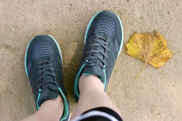 Gambe femminili in scarpe da tennis e foglia gialla, vista ravvicinata dall'alto