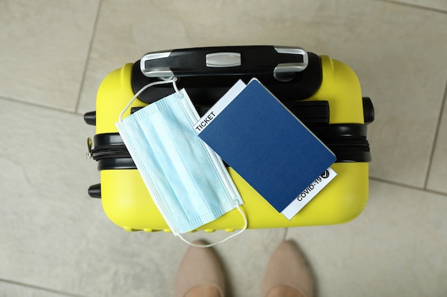 Photo female legs and suitcase with mask and passport with ticket and covid - 19 mark