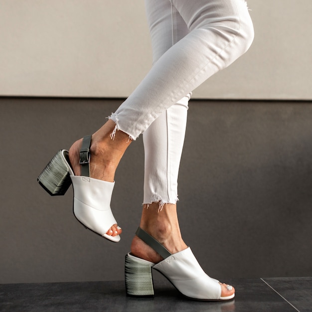 Female legs with stylish white jeans and fashion leather summer shoes near a vintage building on the street. Close-up.