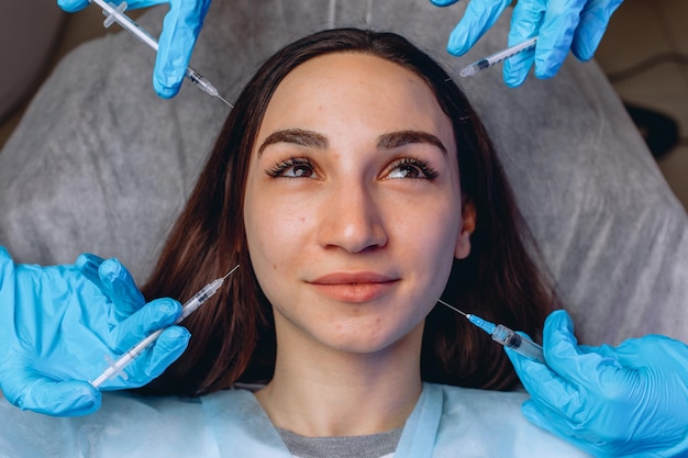 A female looking to the side lying on a chair surrounded by syringes for mesotherapy injections in beauty salon.