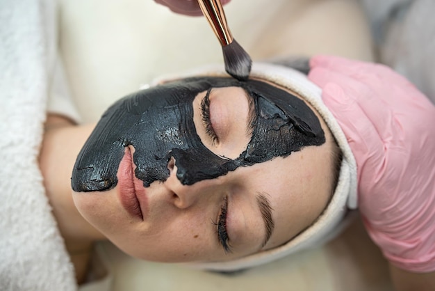 Foto donna che giace male in una clinica termale e riceve una maschera cosmetica nera crema concetto di cura del corpo per la pelle pulita