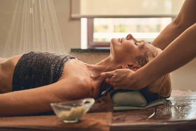 female lying on the wooden desk while having massage in the therapist room