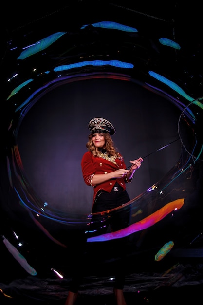女性の魔術師は、黒い背景に、演劇の服を着た奇術師であるシャボン玉でショーを行います。仮装とシルクハットを頭にかぶった女性女優。パフォーマンスの概念。コピースペース