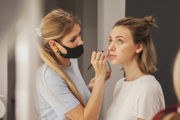 Female makeup artist makes up cute young woman in beauty salon. Customer service in interior salon to create an amazing image. Work make-up creation wizard. Concept of measure satisfaction. Copy space