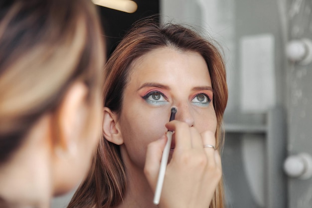 Female makeup artist makes up cute young woman in beauty salon