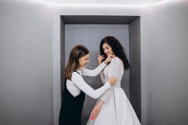 Female making adjustment to wedding gown in fashion designer studio Bride wearing her wedding gown with female dress designer making final adjustments on dress