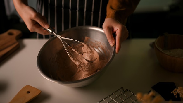 泡だて器を使ってキッチンでクッキーを作る女性がチョコレートクッキー生地を混ぜて準備する