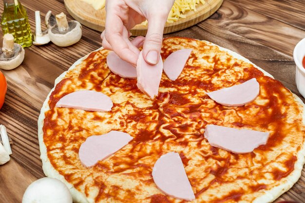 Female making pizza putting cut sausage on the dough with sauce