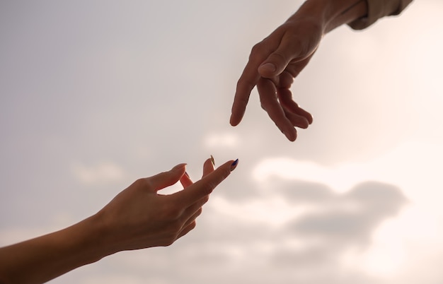 Female and male hand over of the sky. Silhouette of reaching, giving a helping hand, hope and support each other