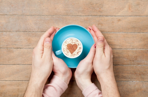 Mani femminili e maschili che tengono tazza di caffè su legno