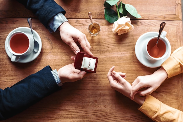 Female and male hands with wedding ring top view, wooden table, rose and cups