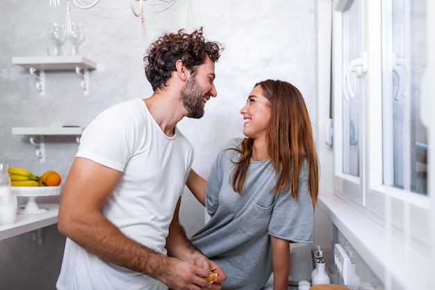 Female and male vegeterians stand together against kitchen interior, prepare salad. Family couple cook on cozy kitchen, husband helps young wife to preapre breakfast for whole family.