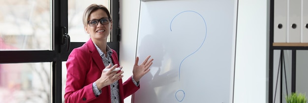 Female manager in glasses standing near whiteboard with question mark in office concept of